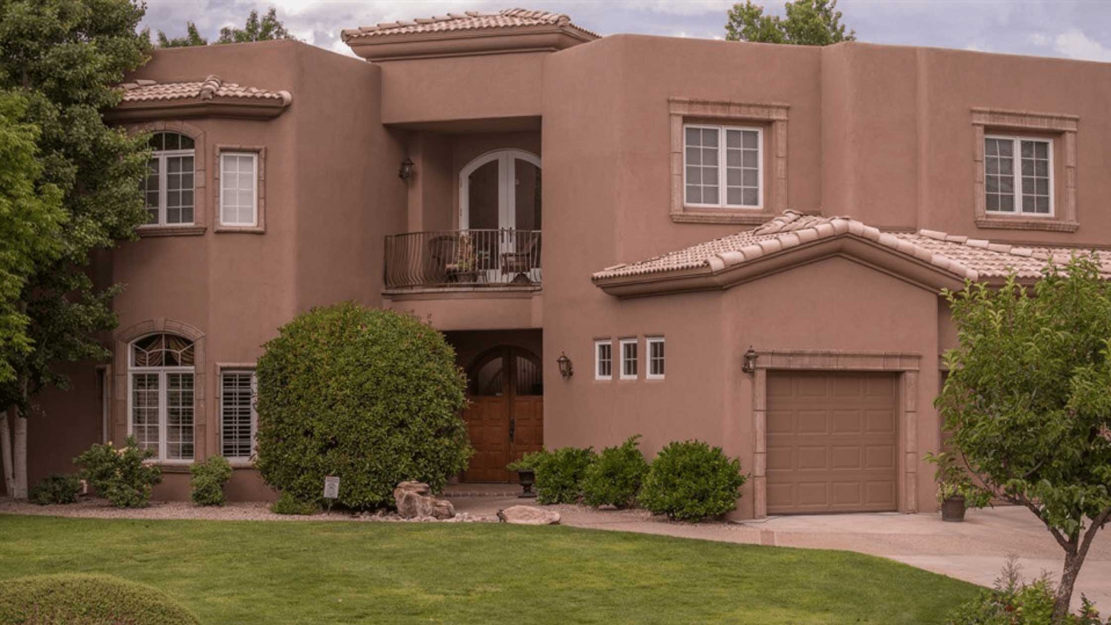 Large two story brown stucco house with green grass